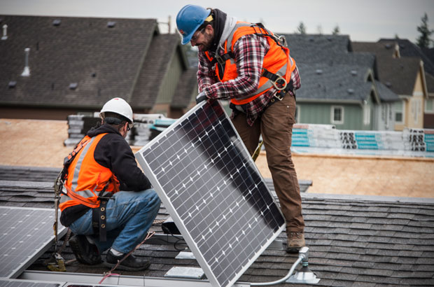 Two workers installing a solar panel on a roof